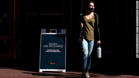 A woman walks by a sign reading &#39;Masks Are Required&#39; outside a shopping mall on August 3, 2021, in San Francisco.