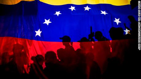 Opposition activists, seen here behind a Venezuelan flag, protest against the deaths of 43 people in clashes with the police during weeks of demonstrations against the government of Venezuelan President Nicolas Maduro, in Caracas on May 17, 2017. 