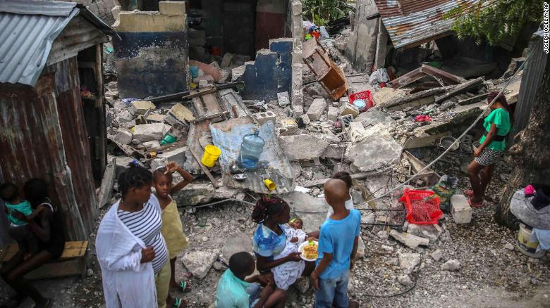 A family eats breakfast in front of homes destroyed by a 7.2 magnitude earthquake in Les Cayes, Haiti, on Sunday, August 15.