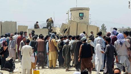 Afghan security guards stand on a wall as hundreds of people gather outside Kabul&#39;s international airport on Tuesday.