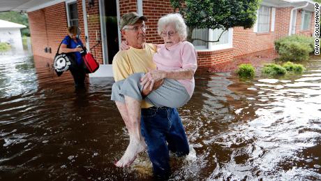 In the aftermath of Hurricane Florence in 2017, Bob Richling carries Iris Darden out of her flooded North Carolina home as her daughter-in-law, Pam Darden, gathers her belongings.