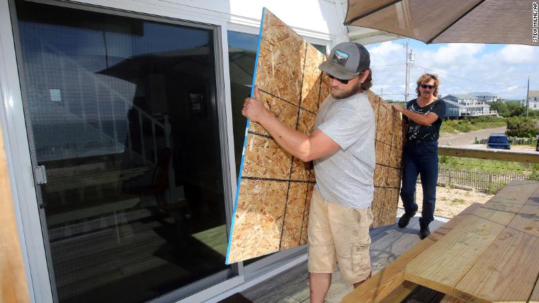 James Masog, center, and Gary Tavares move particle board into place to board up the sliding glass doors of a client&#39;s house in Charlestown, Rhode Island, on Saturday.