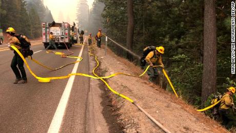 Fire crews carry a hose down a hill as the Caldor Fire burns on both sides of Highway 50 about 10 miles east of Kyburz, California, on  August 26, 2021.