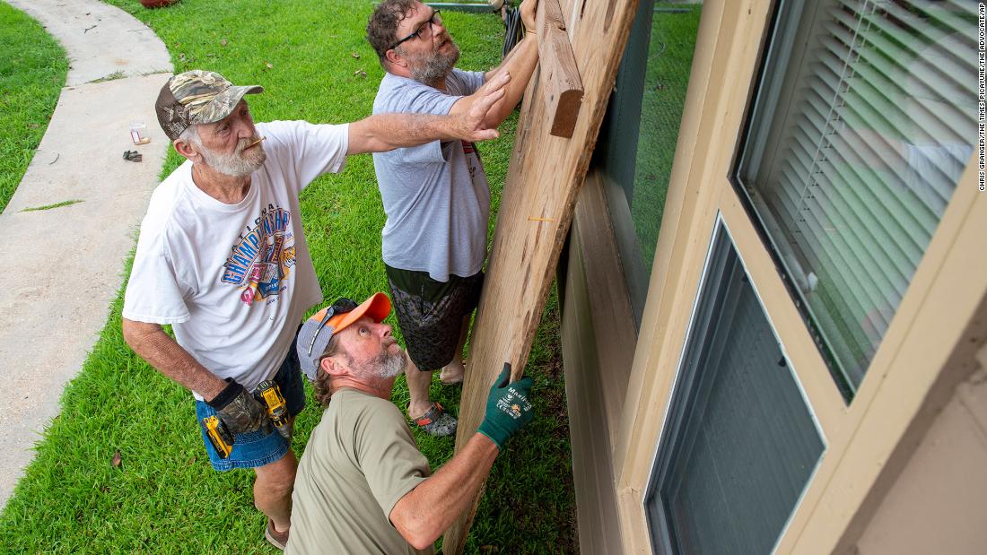 Larry Ackman, bottom, helps neighbor Mike Jackson, left, and his son Cody board up windows in Morgan City, Louisiana.