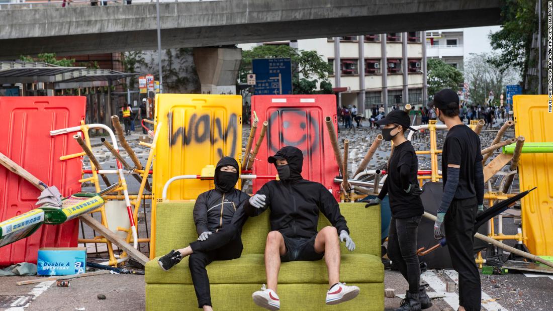 Anti-government protesters sit on a sofa while residents remove barricades built near HKU.