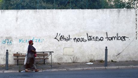 A woman walks past graffiti on a wall reading &quot;State lets us down&quot; in a street in Les Marronniers neighborhood in Marseille in August 2021.
