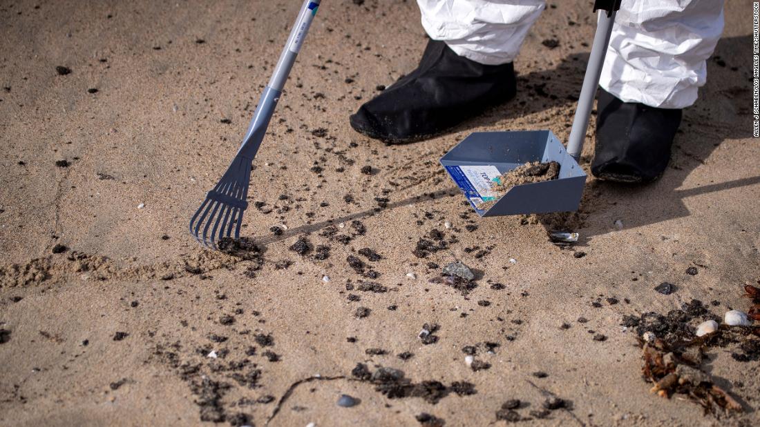 A member of a cleanup crew rakes up some of the oil that washed ashore on Huntington Beach.