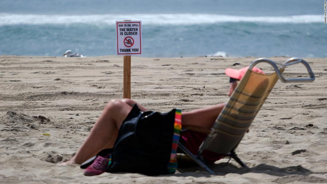 A beachgoer sits in front of a warning sign in Huntington Beach on October 4.
