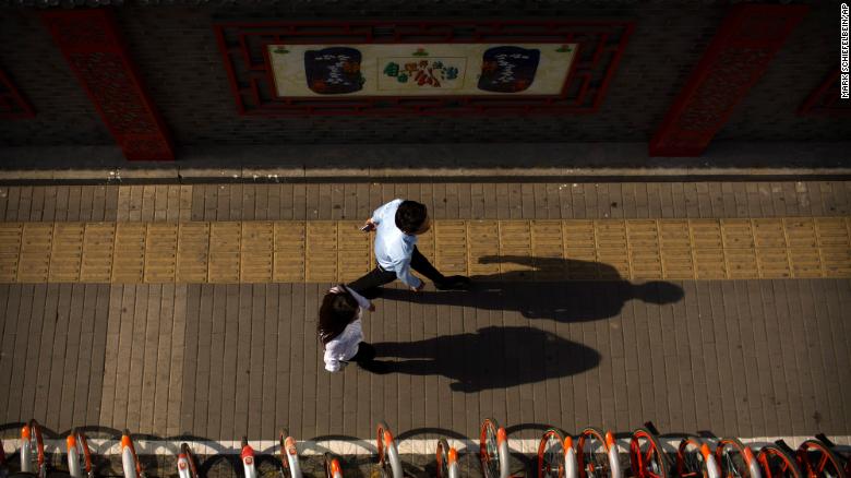 Pedestrians cast shadows as they walk along a sidewalk in Beijing on May 25, 2017.