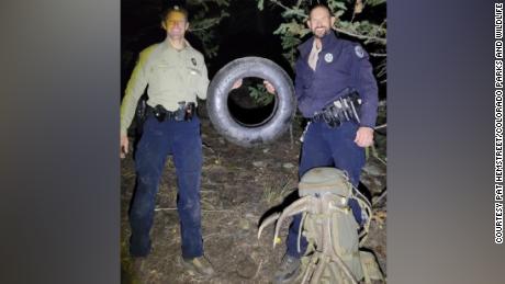 Wildlife officers Murdoch (left) and Swanson (right) hold up the tire that was on this bull elk for over two years.