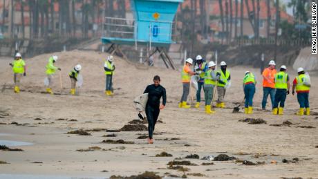 A surfer leaves the water as workers in protective suits clean the contaminated beach in Huntington Beach, California, on October 11. 