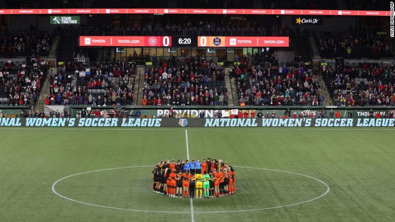 Portland Thorns and Houston Dash players, along with referees, gather at midfield in demonstration of solidarity.