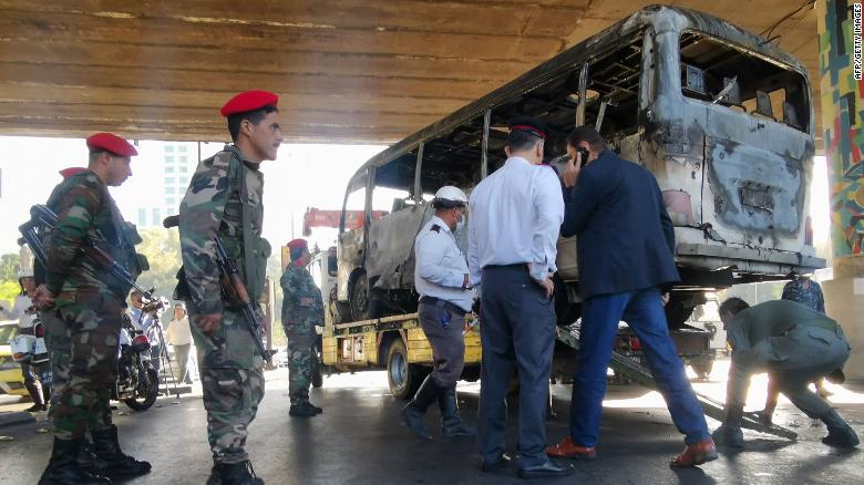 Security forces stand guard as the charred bus is removed from the site of the attack. 