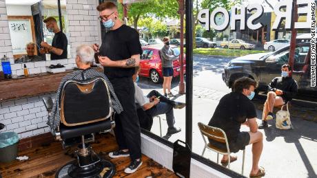 Un peluquero se corta el pelo mientras otros clientes esperan afuera en una cola que comenzó a las 4:30 am en Melbourne el 22 de octubre.