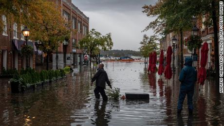 A police officer pulls a potted plant across a flooded street near a bar in Old Town Alexandria.