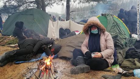 Freezing migrants huddle close to a bonfire at a tent camp on the border. 