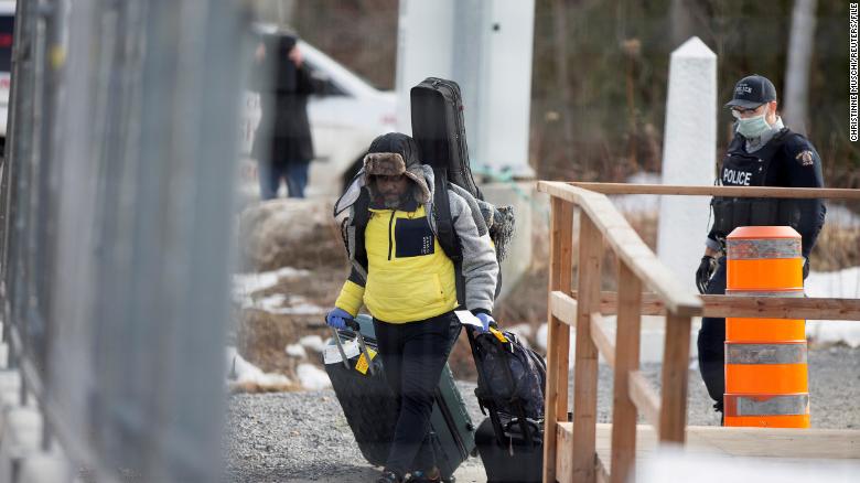An asylum seeker crosses the border from New York into Canada followed by a Royal Canadian Mounted Police (RCMP) officer at Roxham Road in Hemmingford, Quebec, Canada March 18, 2020.