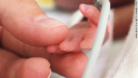 A mother holds the hand of her preterm baby who is in the newborn intensive care unit.