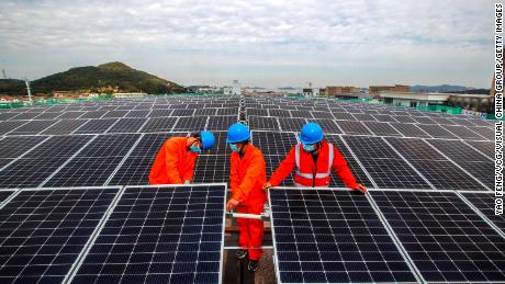 Workers install solar panels on the roof of a fish processing plant in China&#39;s Zhejiang Province in November.