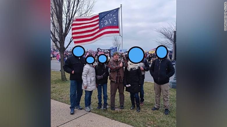 According to a sentencing memorandum, Wrigley posted the this photo where he was standing in a group as he held the 1776 flag aloft to Facebook.  The Department of Justice obscured the faces of the other individuals in the photo. 