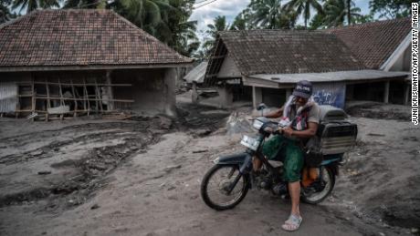A man rides a bicycle beyond damaged houses in Sumber Wuluh village in Lumajang on December 6, 2021.