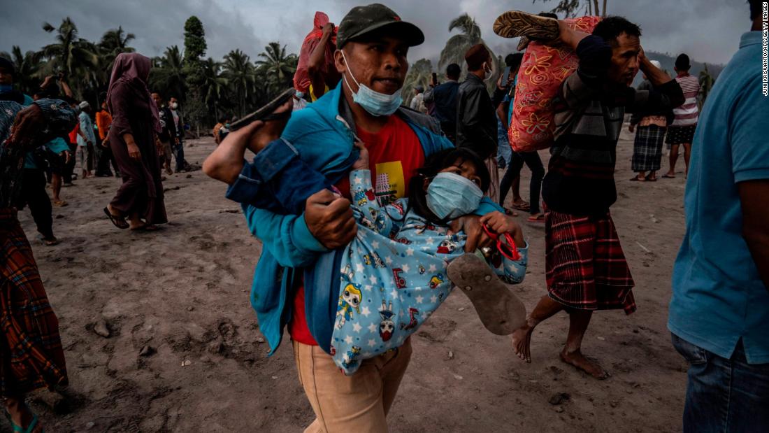 A man carries a child Sunday as other people salvage their belongings from an area covered in volcanic ash at the Sumberwuluh village in Indonesia&#39;s Lumajang district.