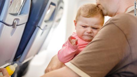 Young tired father and his crying baby daughter during flight on airplane going on vacations.