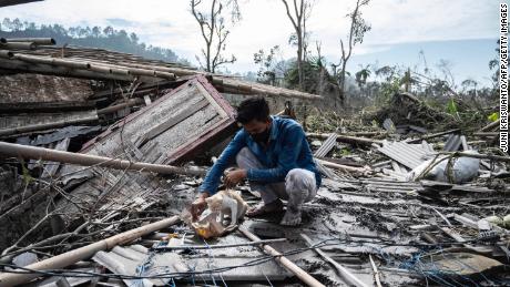 Seorang pria menyelamatkan beberapa barang miliknya dari rumahnya yang rusak di Lumajang pada 8 Desember.