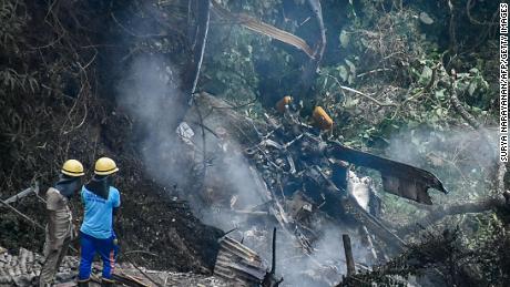 Firemen and rescue workers stand next to the debris of an IAF Mi-17V5 helicopter crash site in Coonoor, Tamil Nadu, on December 8, 2021. - A helicopter carrying India's defence chief General Bipin Rawat crashed, the air force said, with a government minister at the scene saying at least seven people were dead. 