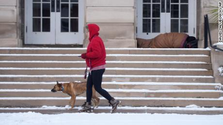 A woman walks a dog Friday as someone seeks shelter on the steps of a church after a storm swept into Denver.