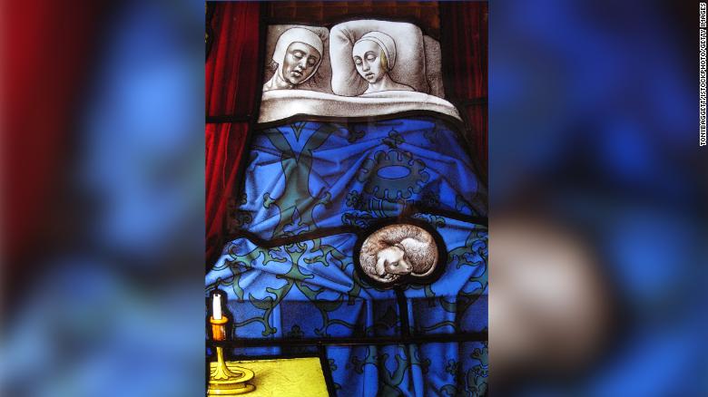 A panel from a medieval stained glass church window depicts a married couple sleeping.