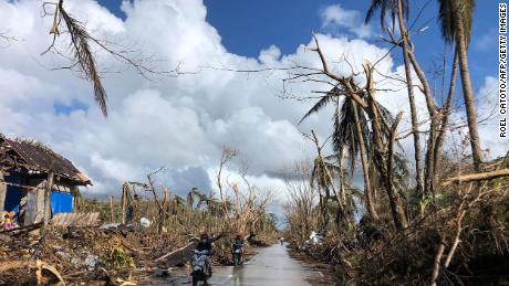 Motorists speed past fallen coconut trees at the height of Super Typhoon Rai along a highway in Del Carmen town, Siargao island on December 20, 2021.