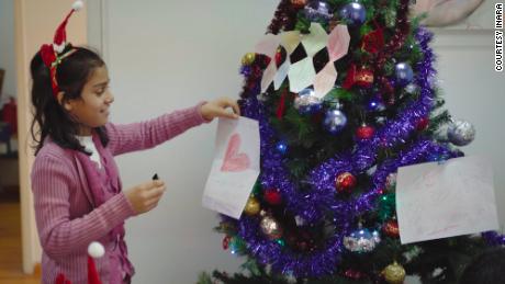 One of INARA&#39;s children places a decoration she made with her holiday wishes written on it onto a Christmas tree.