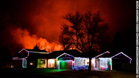 Las luces navideñas adornan una casa mientras los incendios arden de fondo el jueves en Louisville, Colorado.