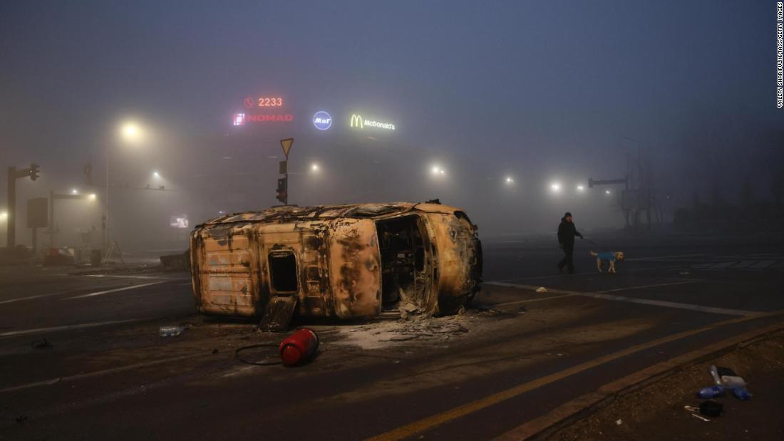 A man walks his dog near a burned-out car in Almaty on January 6.