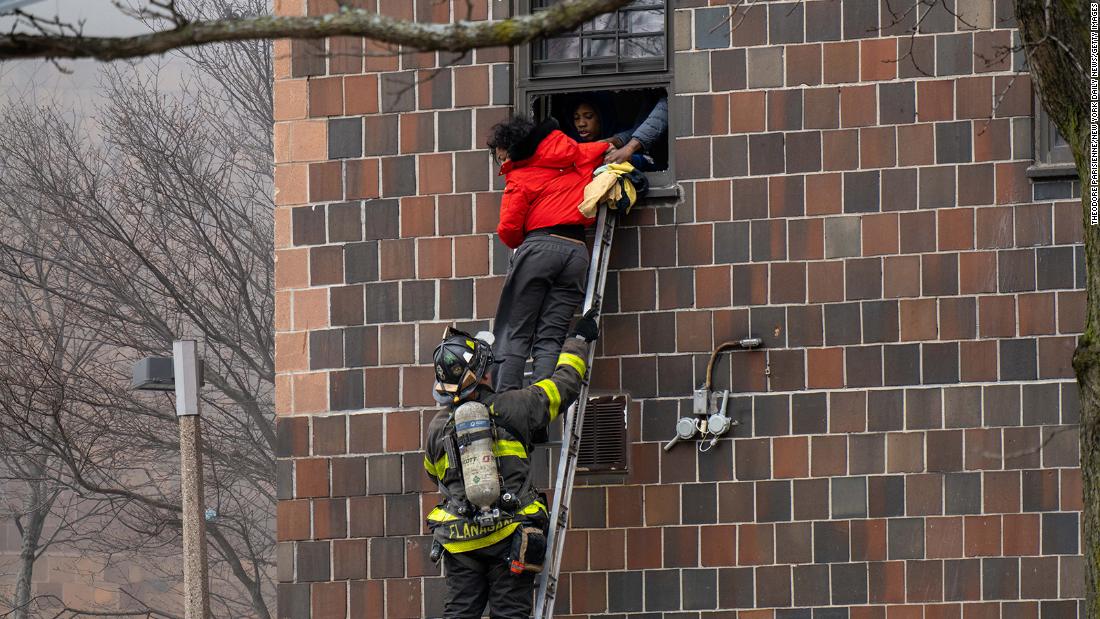 People escape the building through a window as FDNY personnel assist.