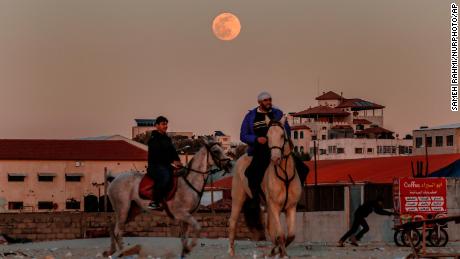 I palestinesi cavalcano su una spiaggia di Gaza mentre la luna del lupo sorge su Gaza City il 17 gennaio.