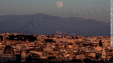 Gli storni volano nel cielo mentre la luna piena sorge sulla città di Roma, in Italia, il 17 gennaio.