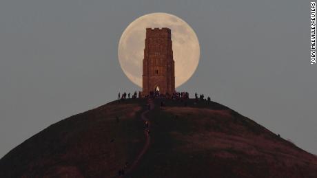 People stand beside St Michael&#39;s Tower as they watch the full moon, sometimes known as a &quot;wolf moon,&quot; rise behind Glastonbury Tor in Glastonbury, England, on January 17.