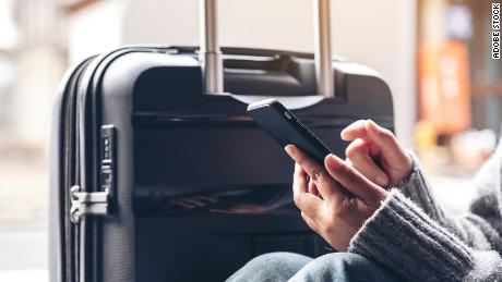 Closeup image of a woman sitting and using mobile phone with a black baggage for traveling