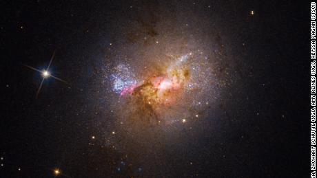 This Hubble Space Telescope image shows the dwarf galaxy Henize 2-10, which is filled with young stars. The bright center, surrounded by pink clouds, indicates the location of its black hole and areas of star birth.