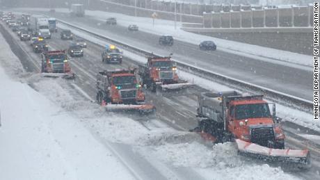 Snowplows line up, from the left side of the road to the right, plowing  accumulated snow on a Minnesota highway.