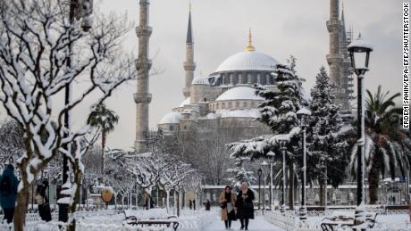 La gente camina frente a la mezquita azul cubierta de nieve en Estambul.