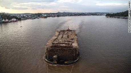 A barge filled with logged timber pulled along the Mahakam river passes the town of Samarinda, East Kalimantan on November 4, 2021. 