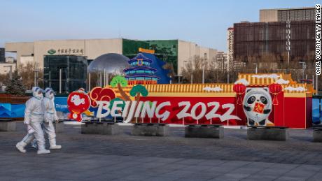 People wearing personal protective kits walk past a Winter Olympics display in Beijing on Wednesday.
