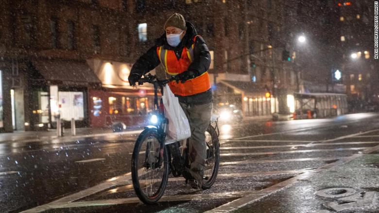 A food delivery driver on a bicycle rides in the snow on Friday in New York City.