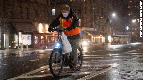 A food delivery driver on a bicycle rides in the snow on Friday in New York City.