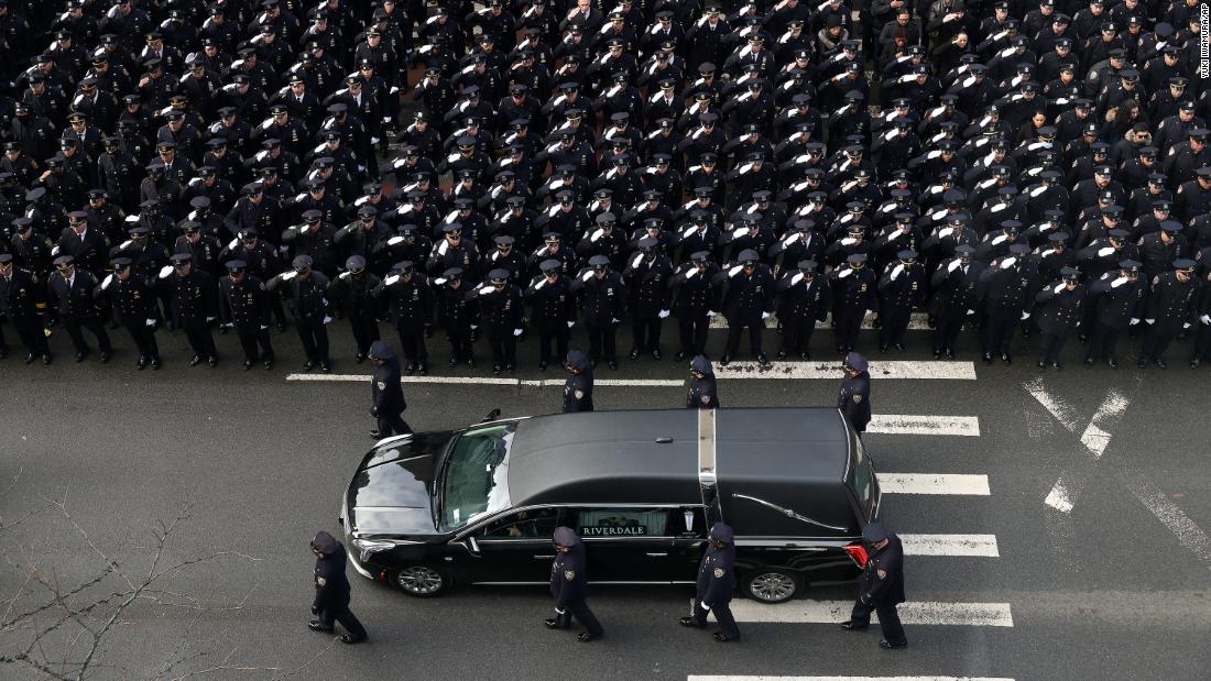 Police salute as a hearse carries Mora&#39;s casket down Fifth Avenue.