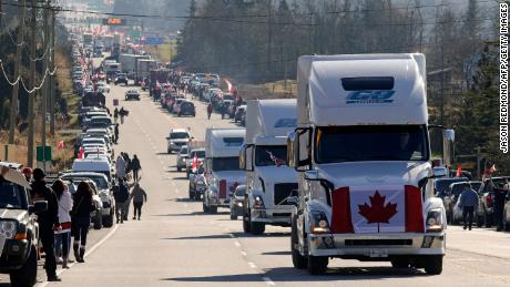 Trucks with Canadian flags drive by anti-vaccine mandate and anti-government protesters Saturday in Surrey, British Columbia, near the border with Washington state. 