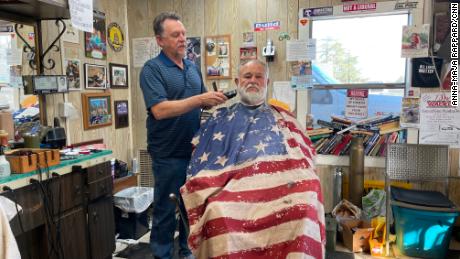 Woody Clendenen drapes his clients in an American flag cape before cutting their hair in his barber shop.